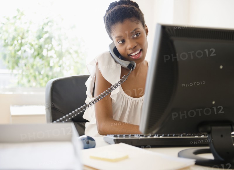 Black businesswoman talking on phone and using laptop