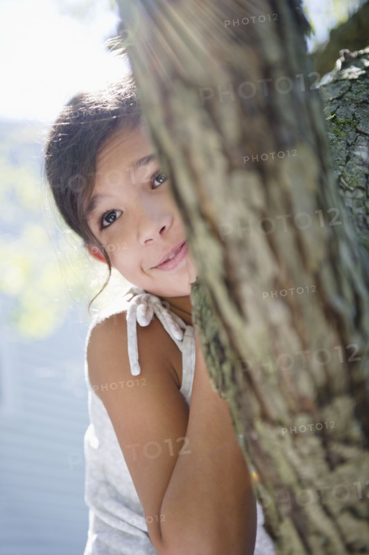 Hispanic girl hiding behind tree
