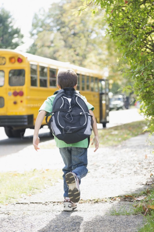 Caucasian boy running after school bus