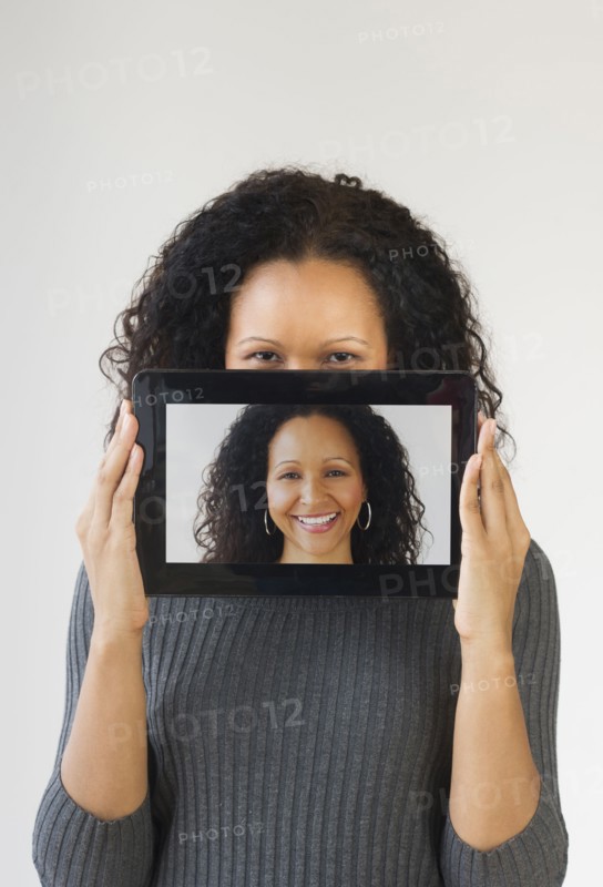 Hispanic woman holding digital tablet in front of face