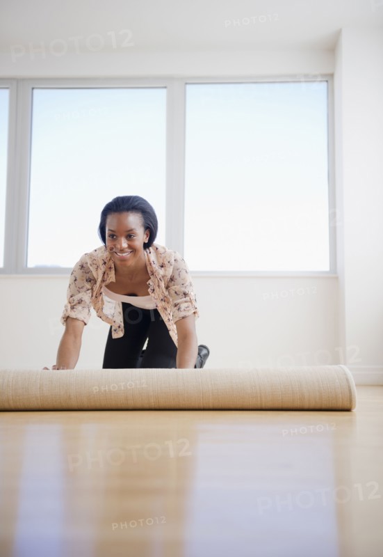 Black woman unrolling carpet in new home