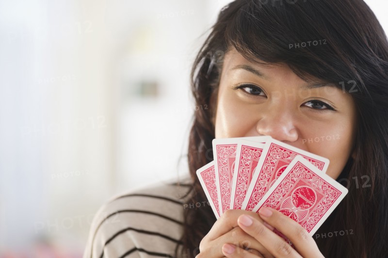 Pacific Islander woman covering her mouth with playing cards