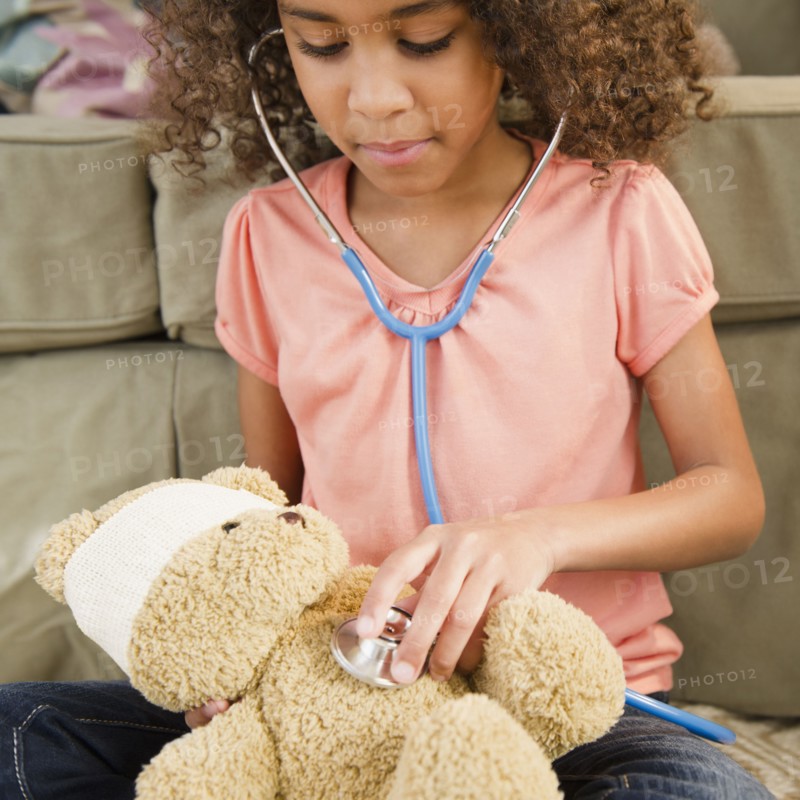 Mixed race girl using stethoscope on teddy bear