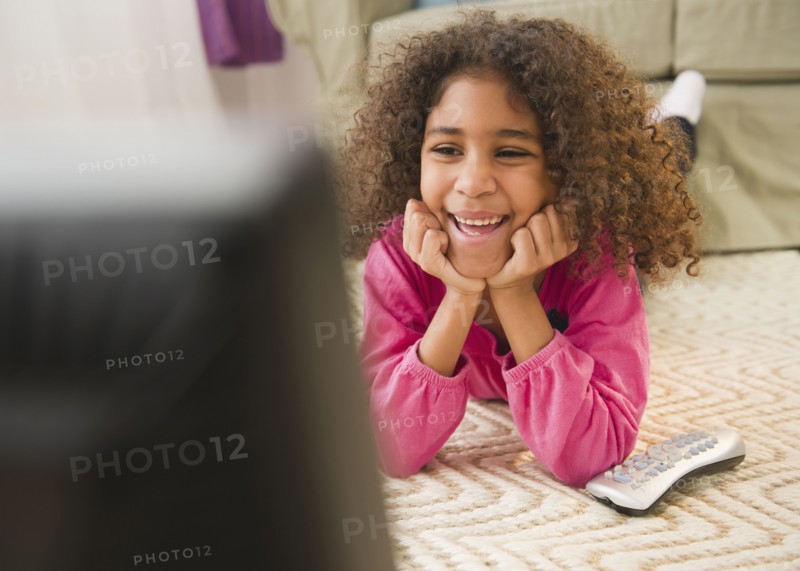 Mixed race girl laying on floor watching television