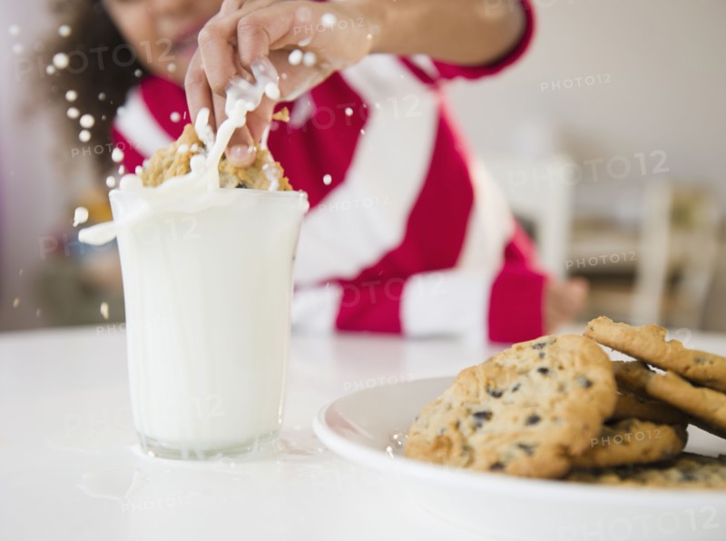 Mixed race girl dunking cookie into milk