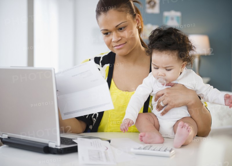 Mixed race mother holding baby and paying bills