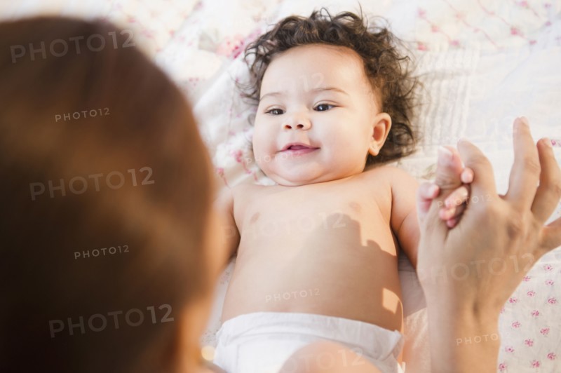Mixed race mother holding hands with baby