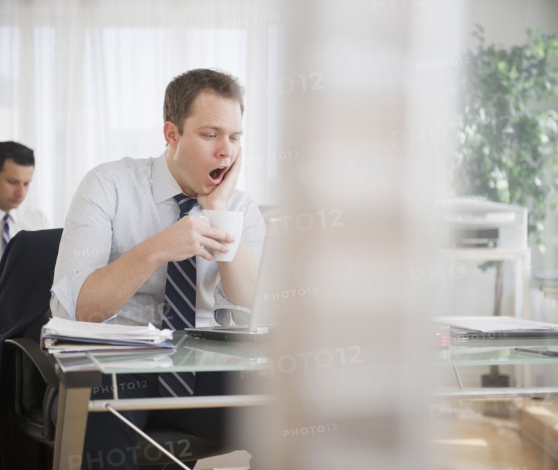 Caucasian businessman drinking coffee and yawning