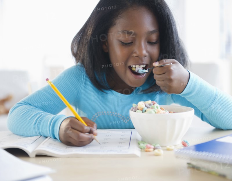 Black girl eating cereal and writing in workbook