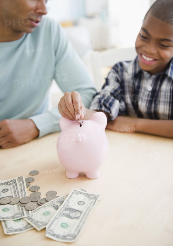 Father watching son put coin in piggy bank