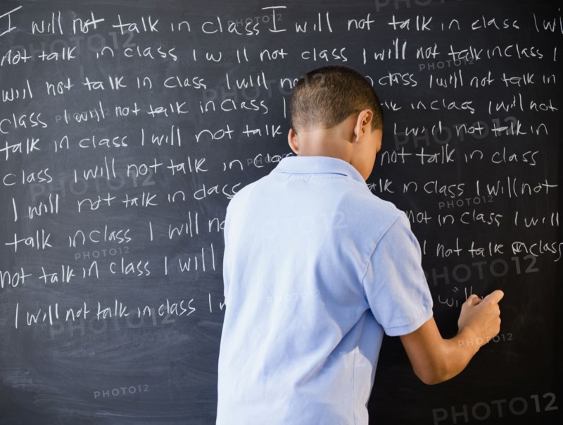 Hispanic boy writing punishment on blackboard