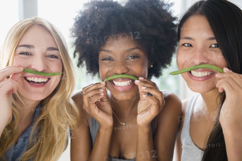 Smiling women using green beans as mustaches