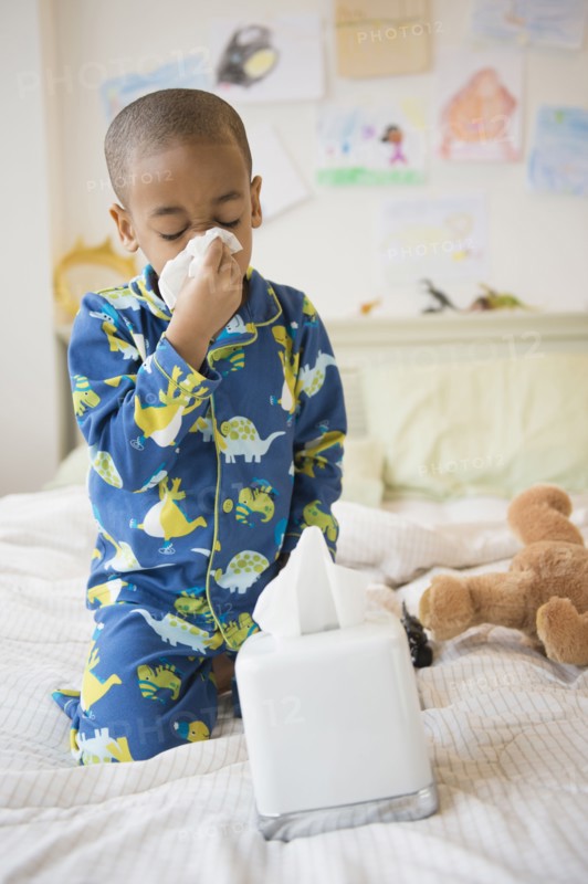 African American boy blowing his nose on bed
