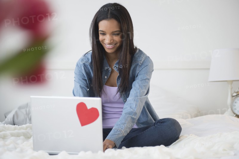 Mixed race woman using laptop on bed