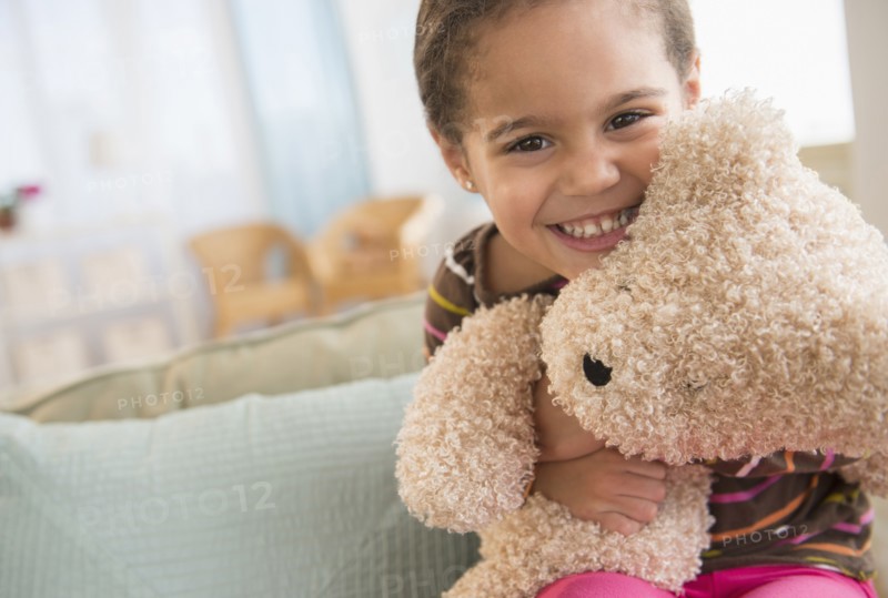 Hispanic girl hugging teddy bear on sofa