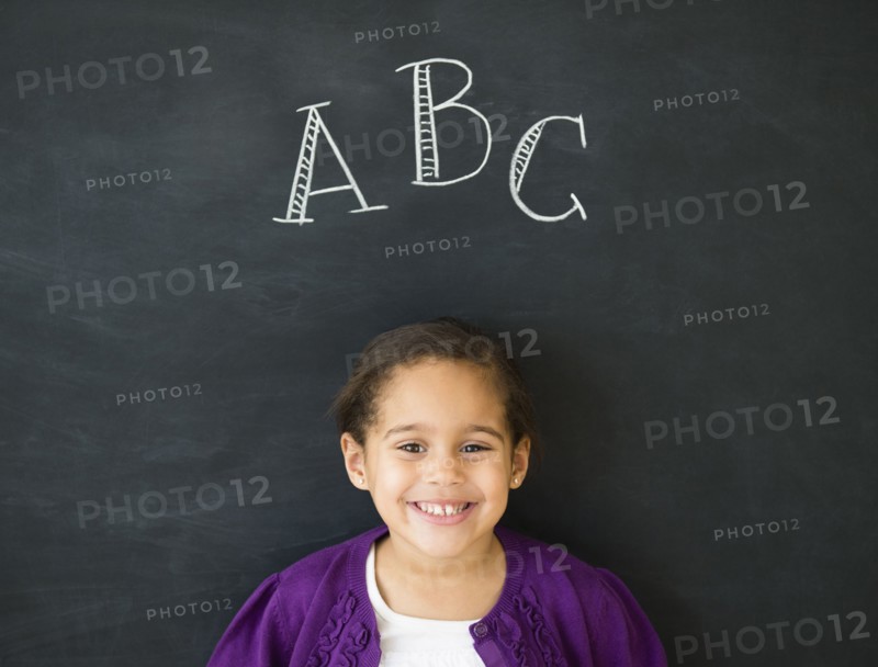Hispanic girl standing under 'ABC' on chalkboard
