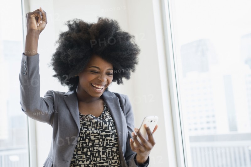 Mixed race businesswoman holding cell phone and cheering
