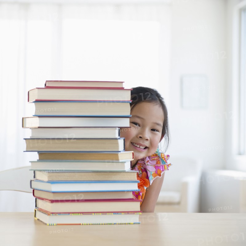 Korean girl peeking from behind stack of books