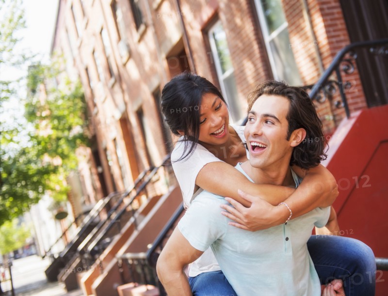 Man carrying girlfriend piggyback outside brownstones