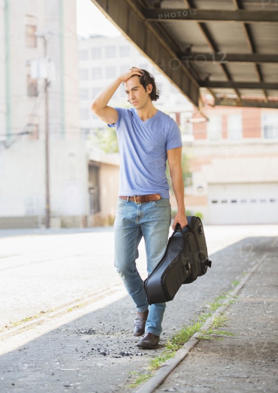 Caucasian man carrying guitar case on city street