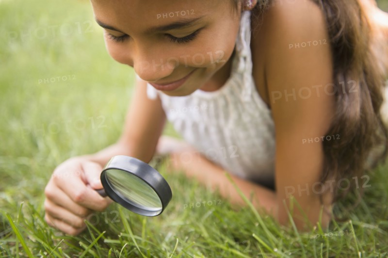 Mixed race girl using magnifying glass in grass