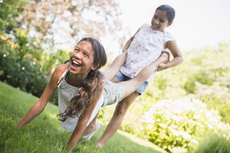 Mixed race girls playing wheelbarrow in backyard