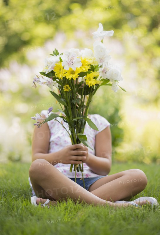 Mixed race girl holding bouquet of flowers in grass