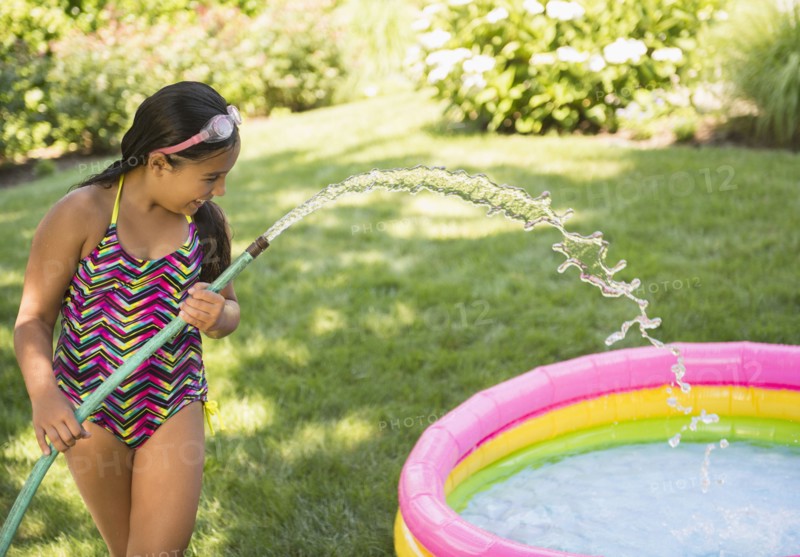Mixed race girl filling wading pool in backyard