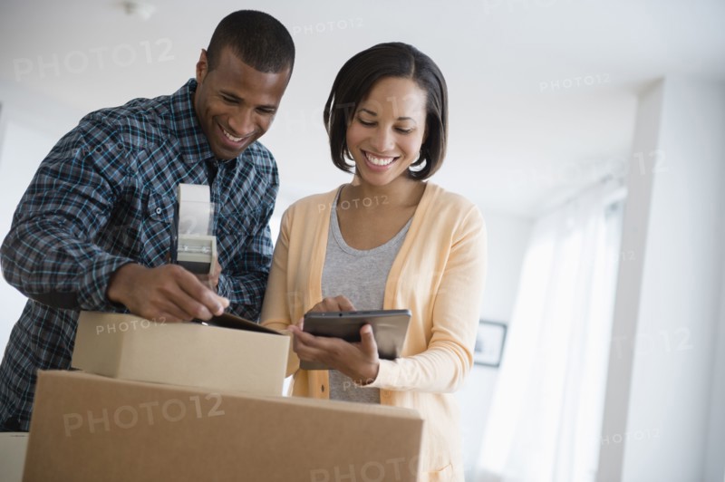 Couple with digital tablet taping up moving boxes