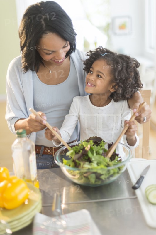 African American mother and daughter tossing salad