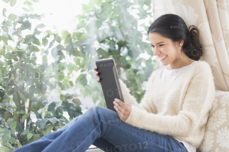 Hispanic woman using digital tablet at window seat