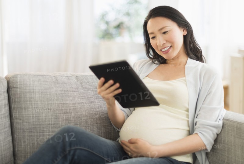 Pregnant Japanese woman using digital tablet on sofa