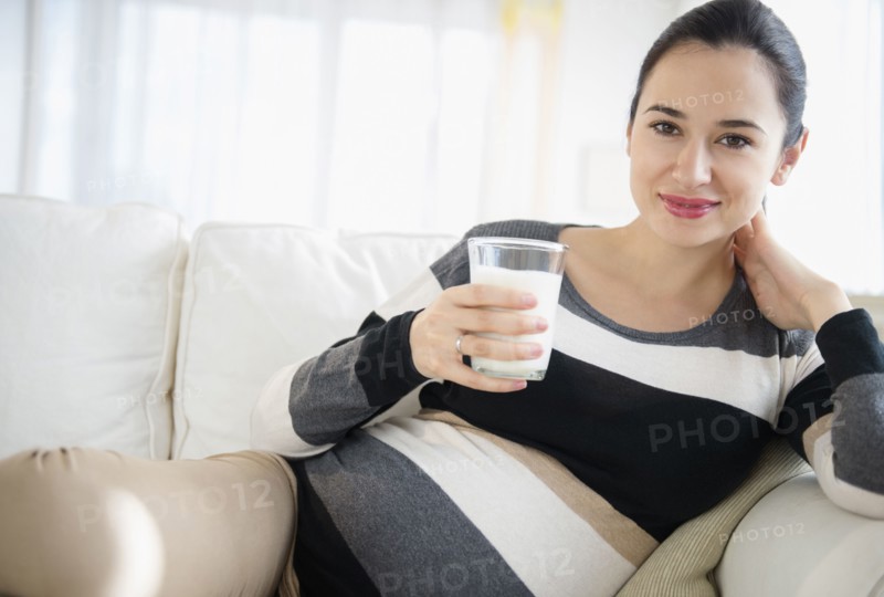 Pregnant Caucasian woman drinking milk on sofa