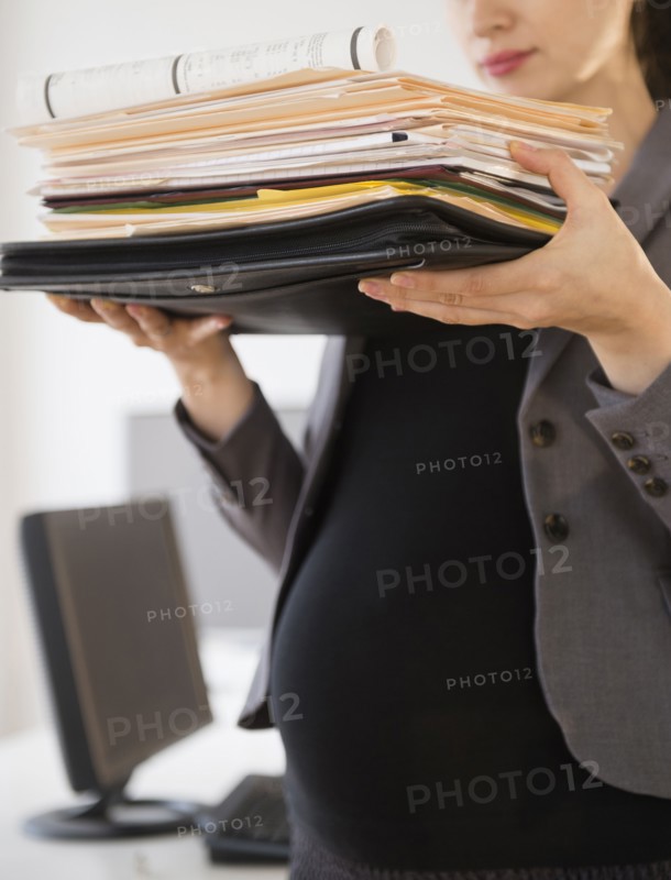 Pregnant Caucasian businesswoman carrying folders in office