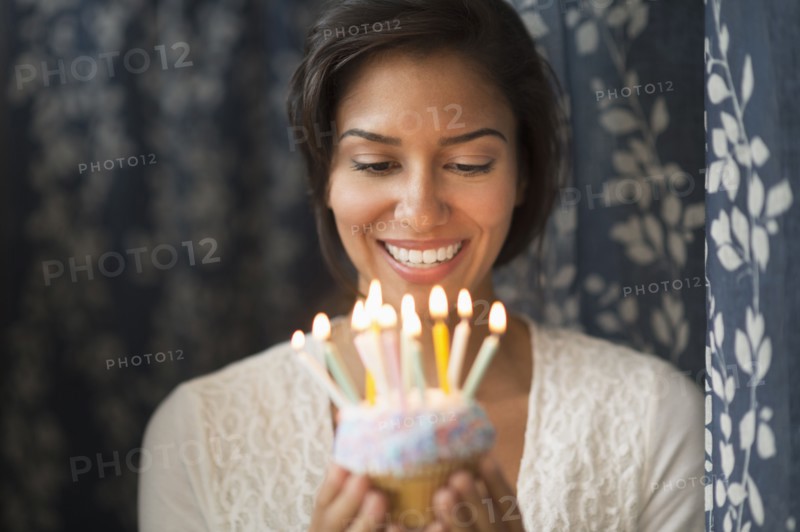 Hispanic woman looking down at lit candles on birthday cupcake