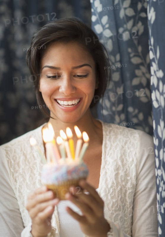 Hispanic woman looking down at lit candles on birthday cupcake