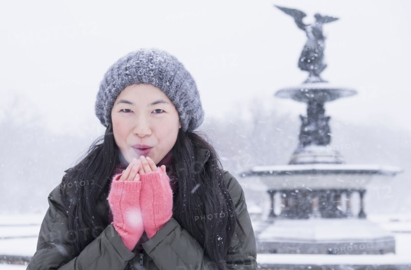 Asian woman blowing on hands in snow