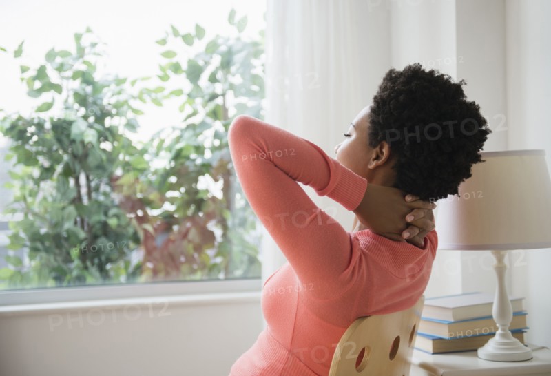 Black woman relaxing at window with hands behind head