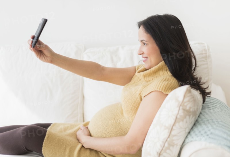 Pregnant Hispanic woman taking picture with cell phone