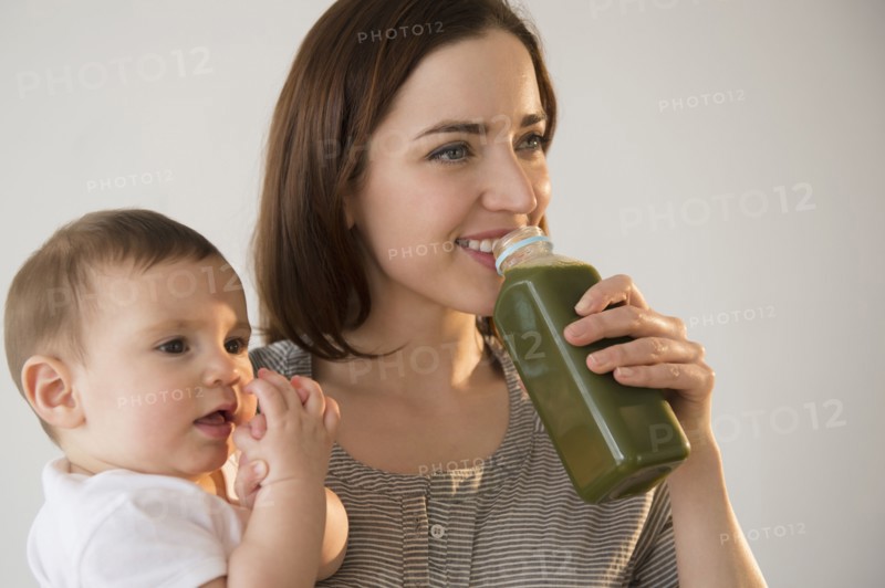 Mother holding baby and drinking green juice
