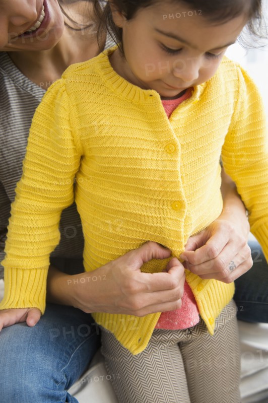 Hispanic mother buttoning daughter's sweater