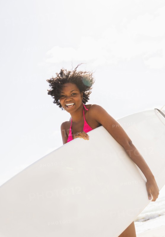 African American woman carrying surfboard on beach