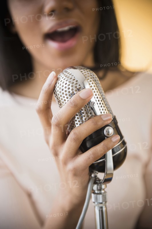Mixed race woman singing into vintage microphone