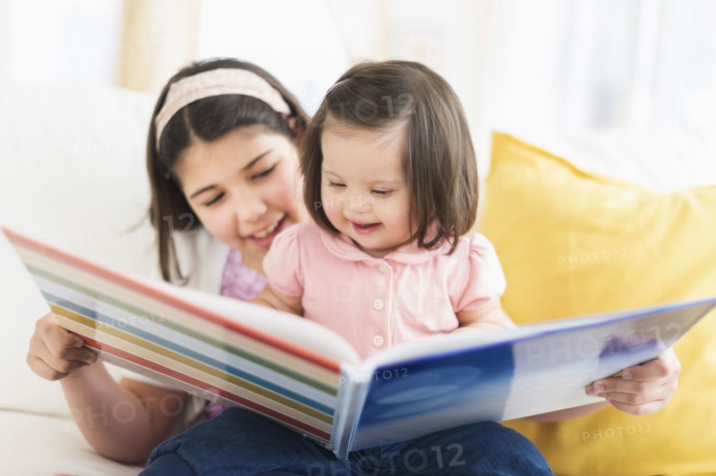 Hispanic girl reading to toddler sister in living room