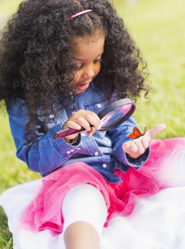 Mixed race girl examining butterfly with magnifying glass