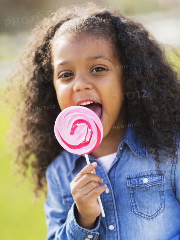 Mixed race girl licking lollipop outdoors