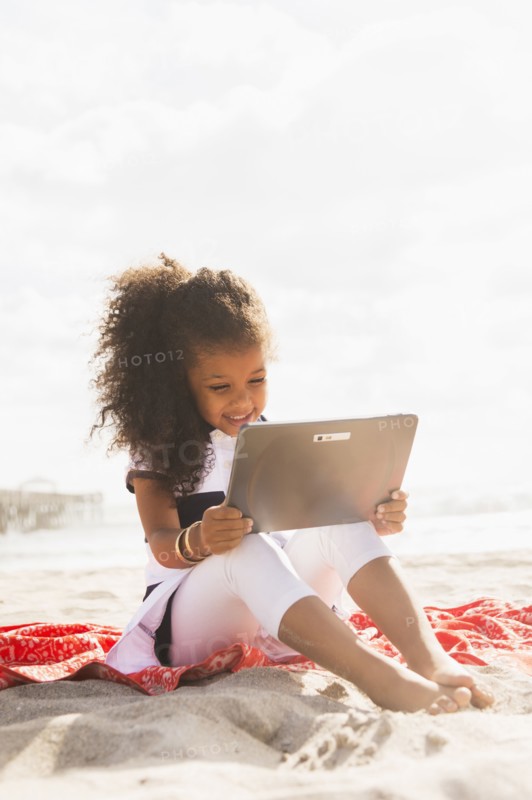 Mixed race girl using digital tablet on beach