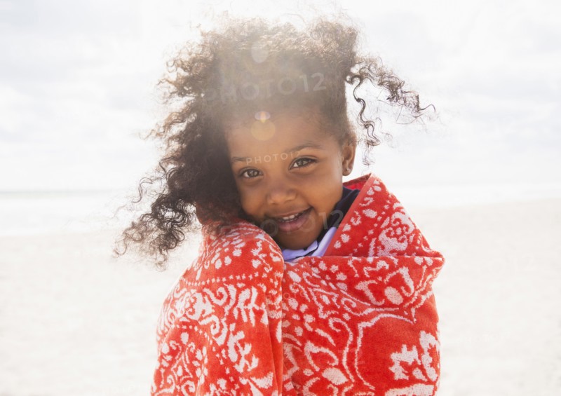 Mixed race girl wrapped in towel on beach