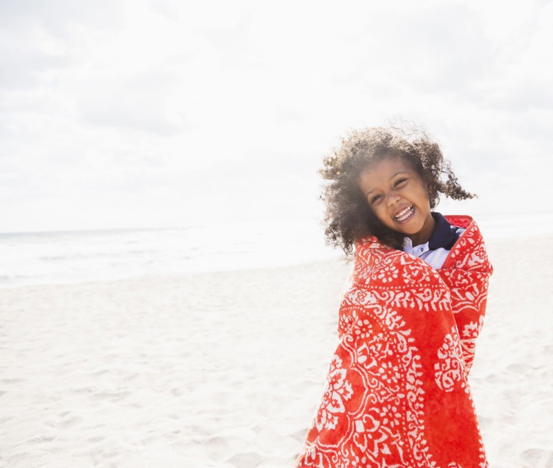 Mixed race girl wrapped in towel on beach