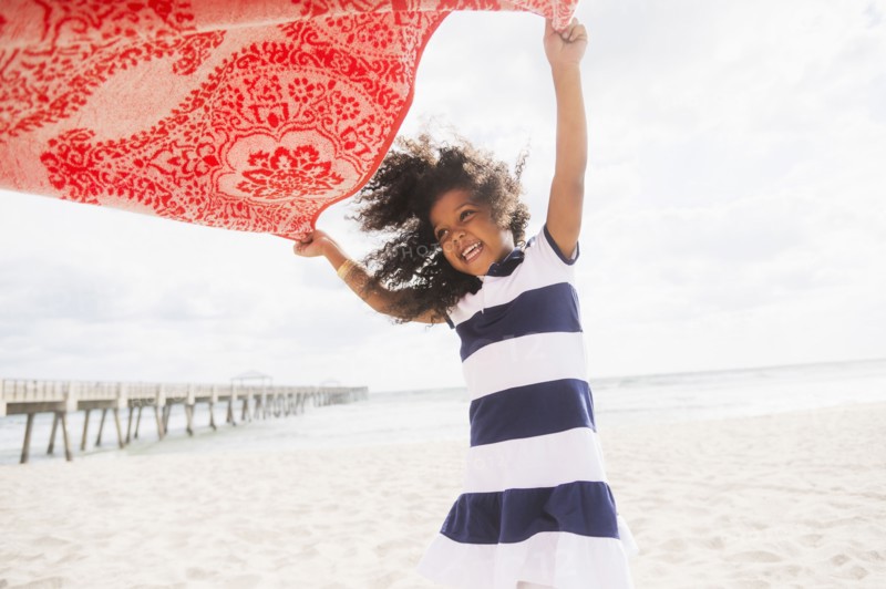 Mixed race girl playing with towel on beach